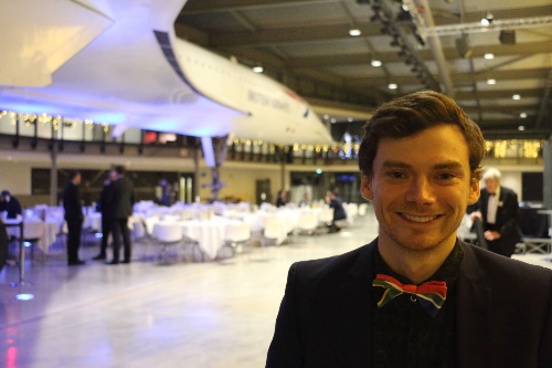 University of Bristol student Franco Labia smiles in front of Concorde. They are wearing a bowtie with the flag of their native South Africa on it.